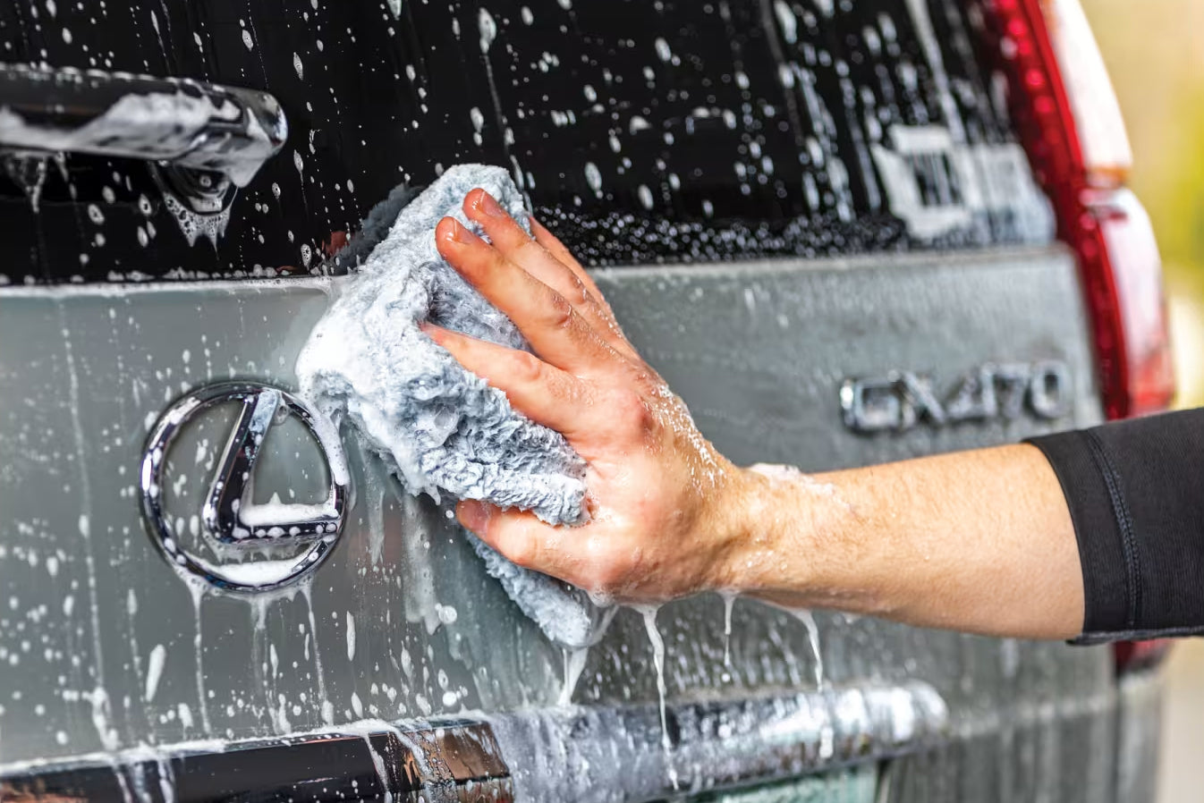Person cleaning a Lexus car with a soapy cloth