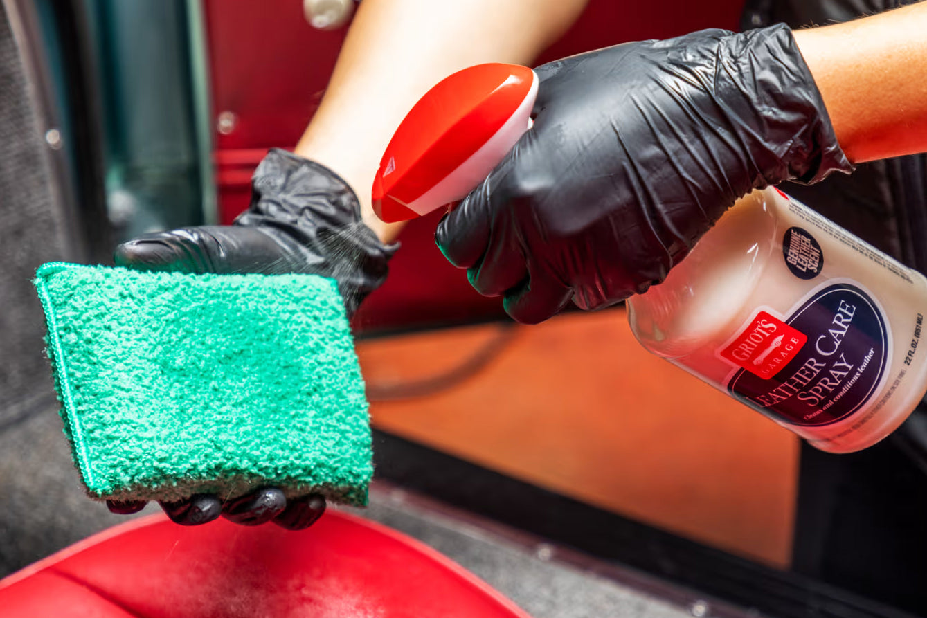 Person cleaning car interior with a green sponge, red brush, and bottle of Windex.