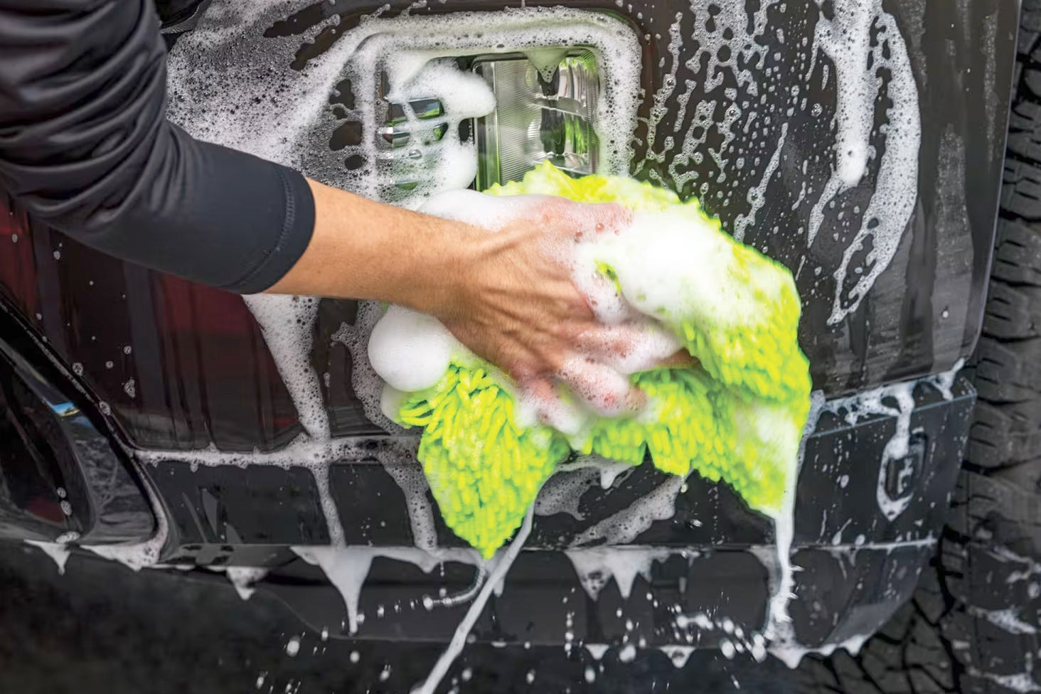 Person washing a car with a soapy green towel