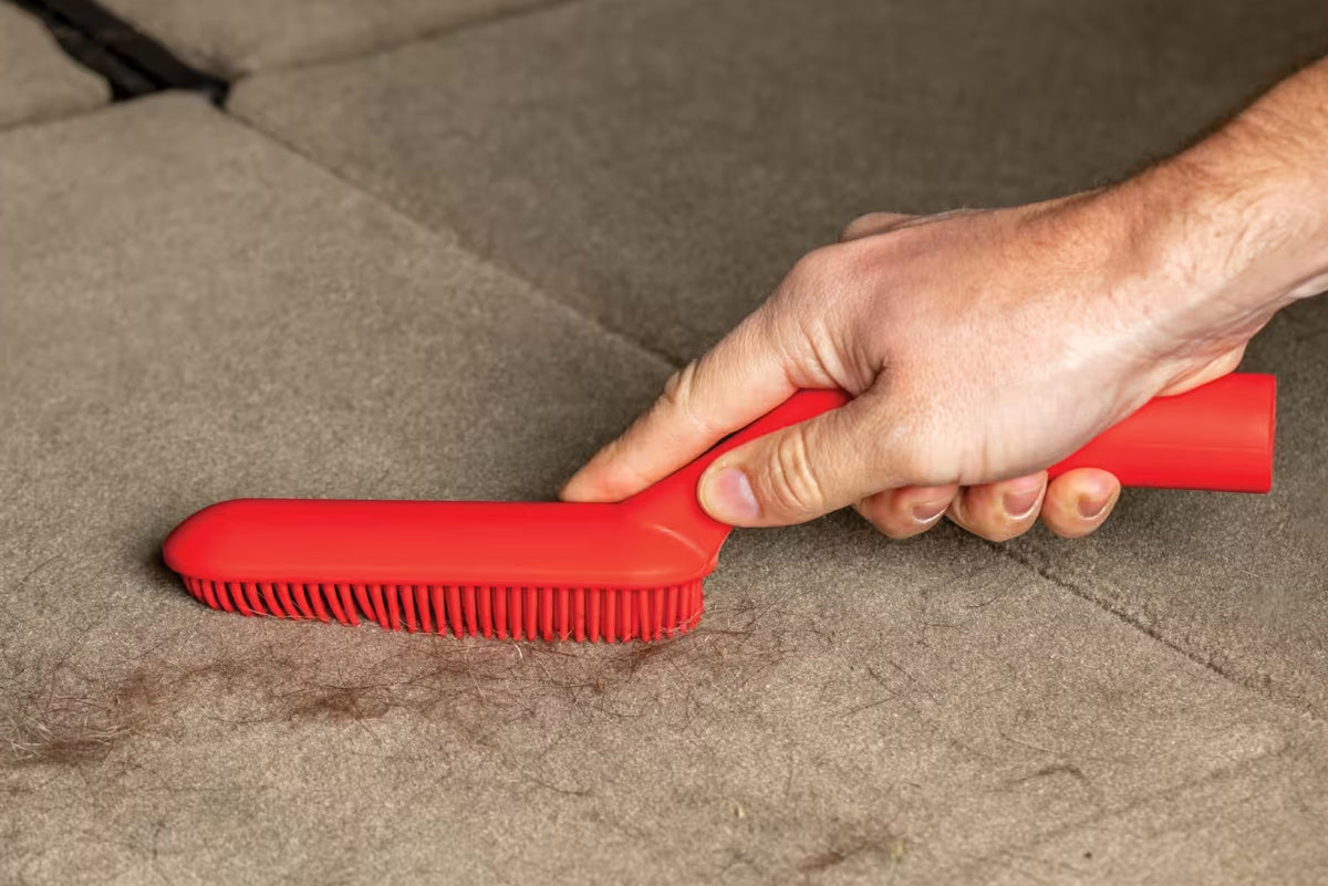Red brush being used on a carpet by a person's hand