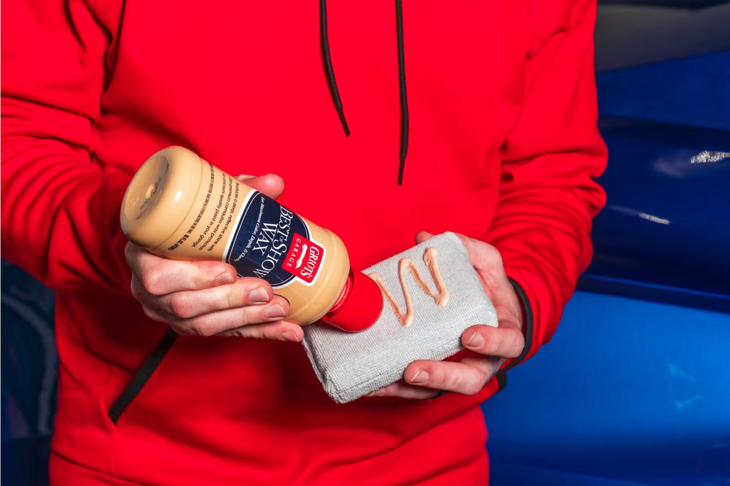A person using a grey microfiber cloth to apply car wax