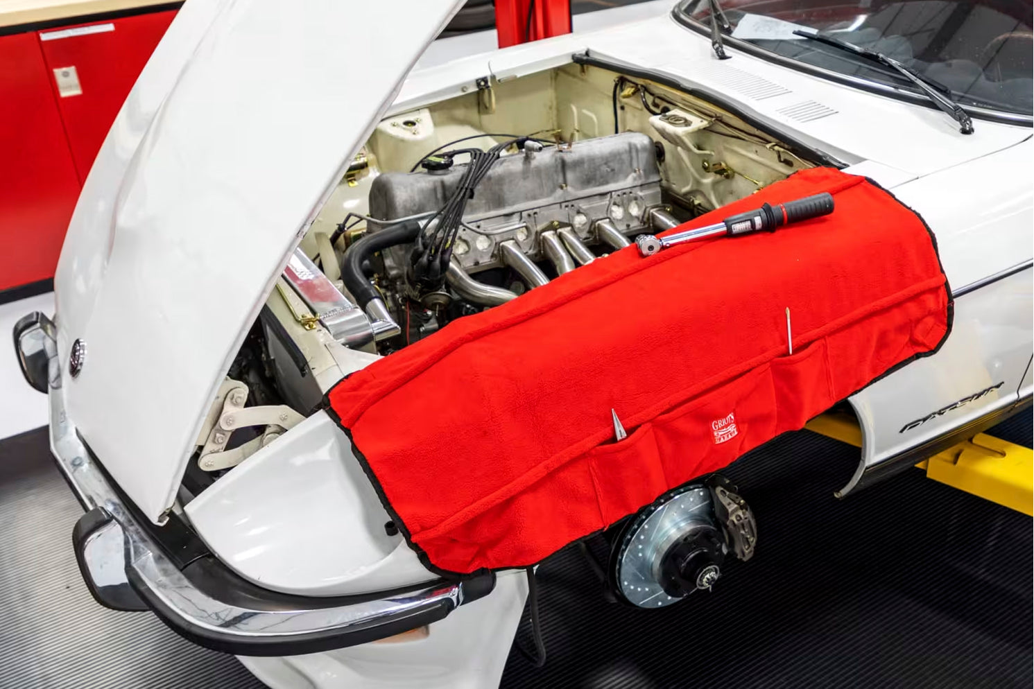 A red fender cover applied over the fender of a white car in a garage setting