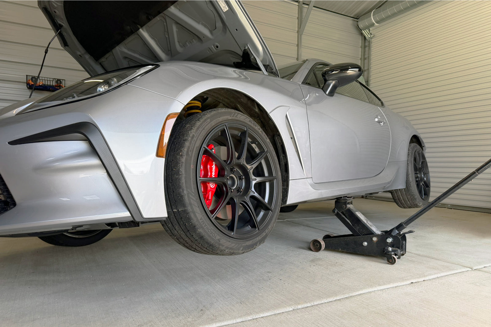 Silver sports car with open hood on a concrete floor in a garage using the PERRIN Center Mount Jack Pad to lift car.