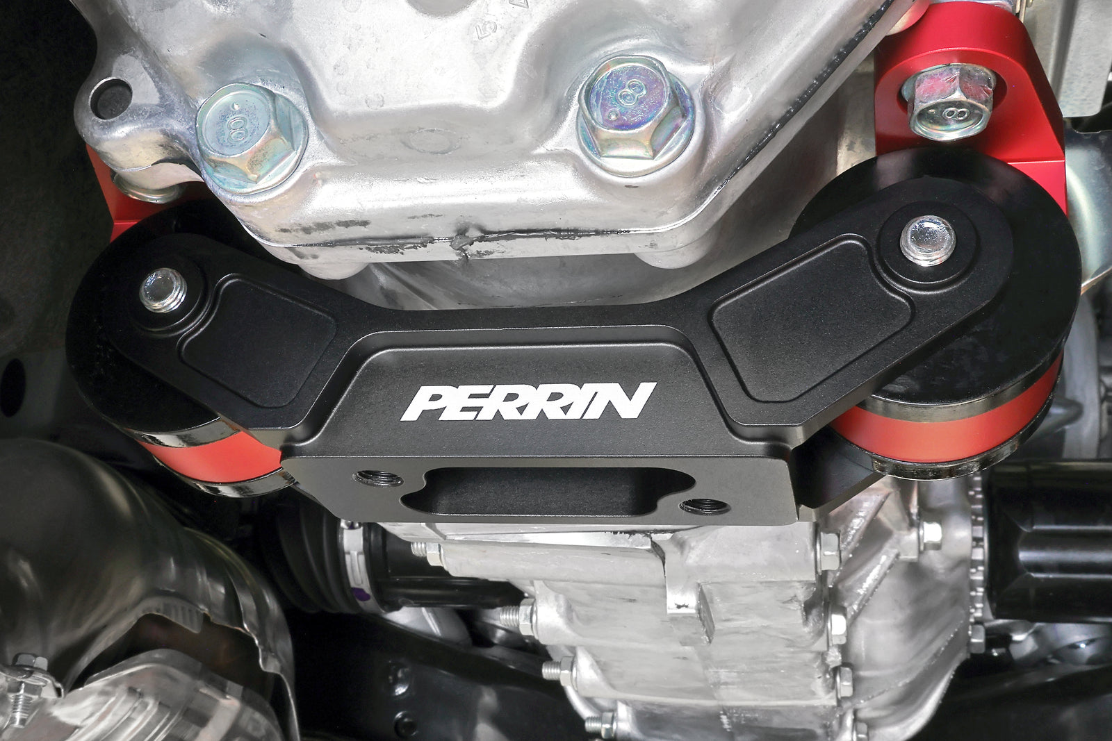 PERRIN Transmission Mount installed on Subaru transmission, undercarriage view showing black billet bracket and red anodized bases