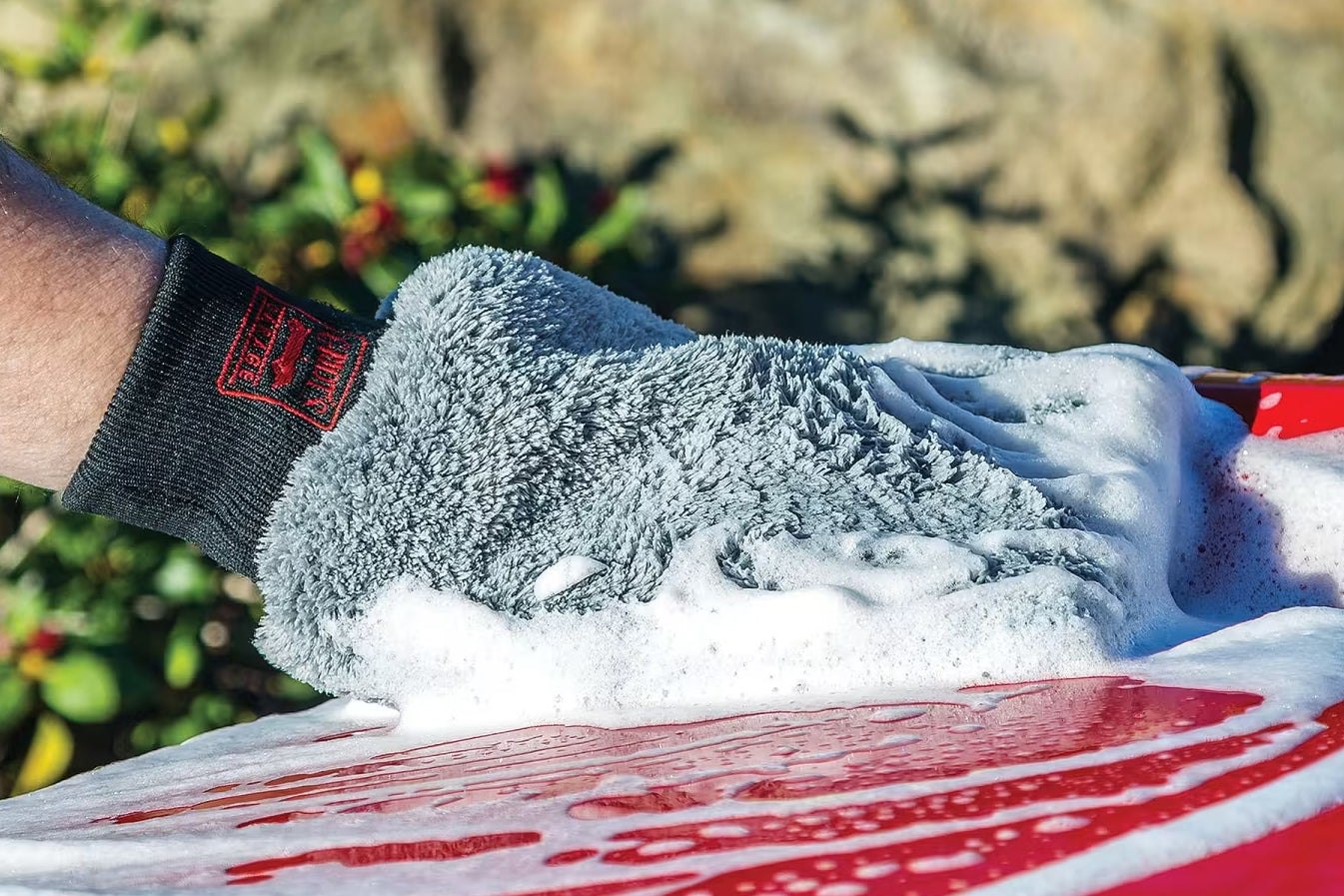 Person cleaning a car with a gray sponge outdoors