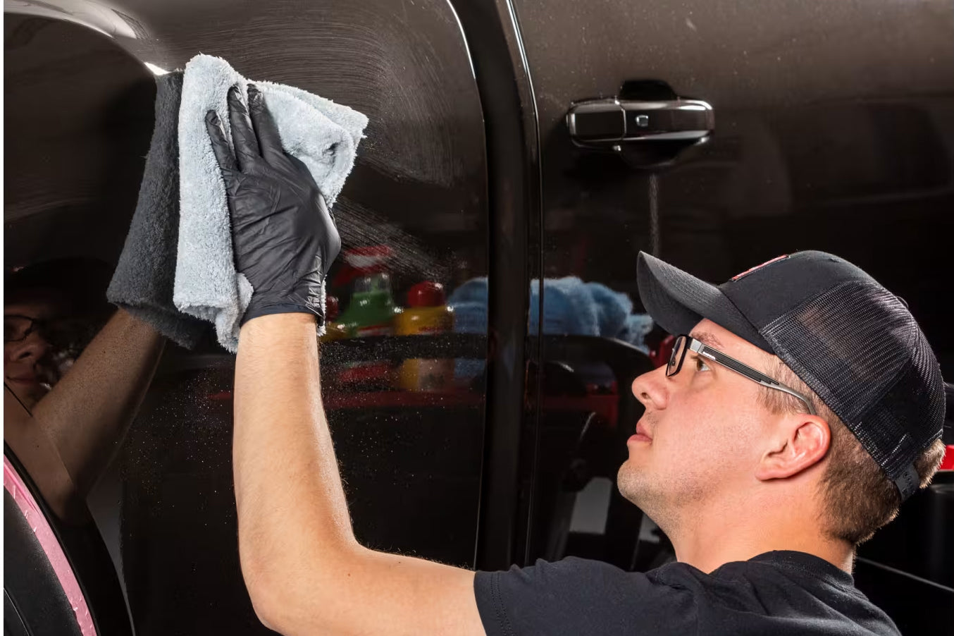 Person cleaning a car window with a cloth, wearing a cap and gloves.