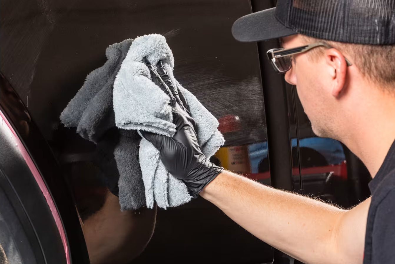 Person cleaning a car window with a gray towel and black gloves