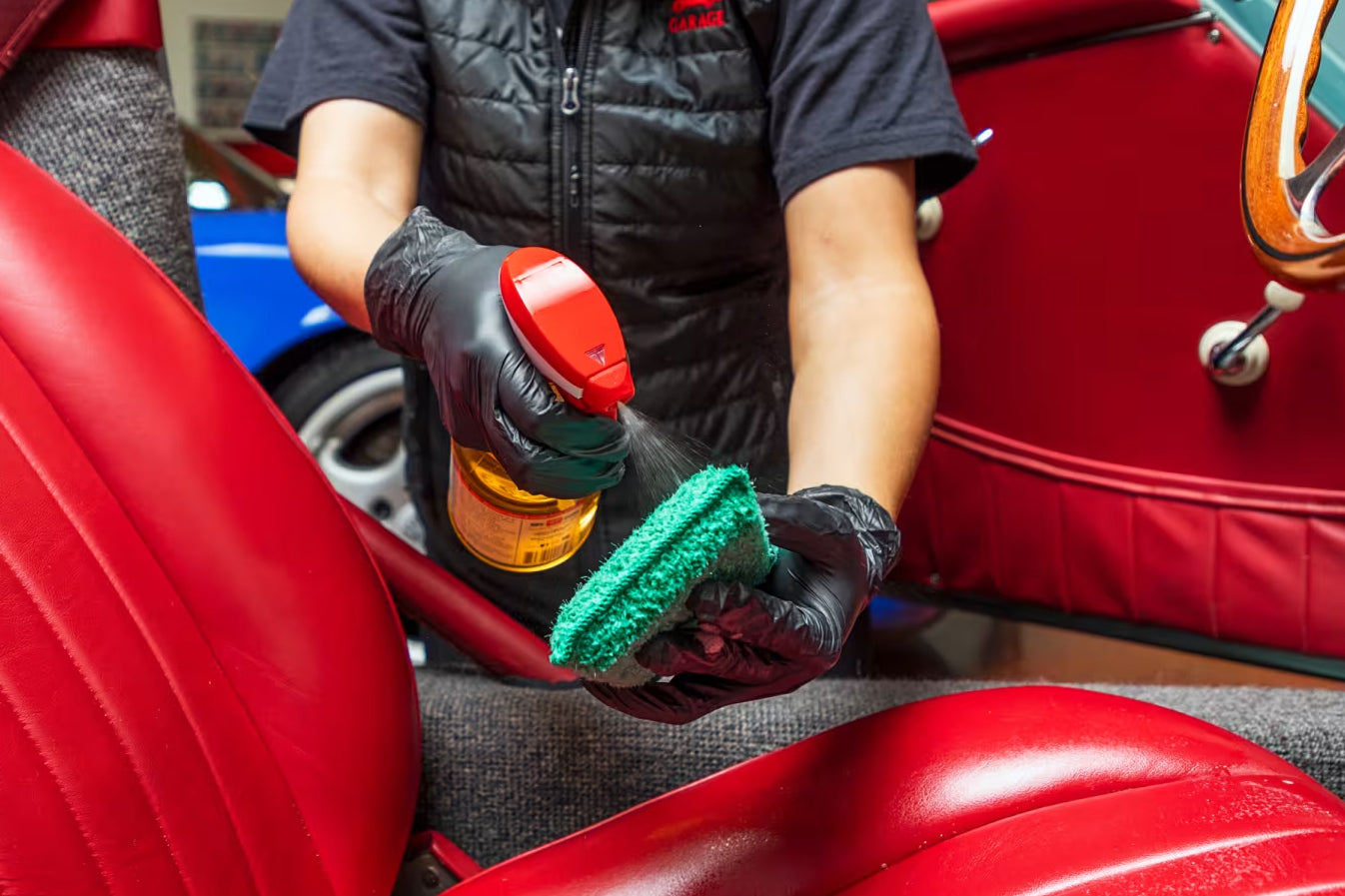 Person cleaning a red car seat with a spray bottle and cloth.