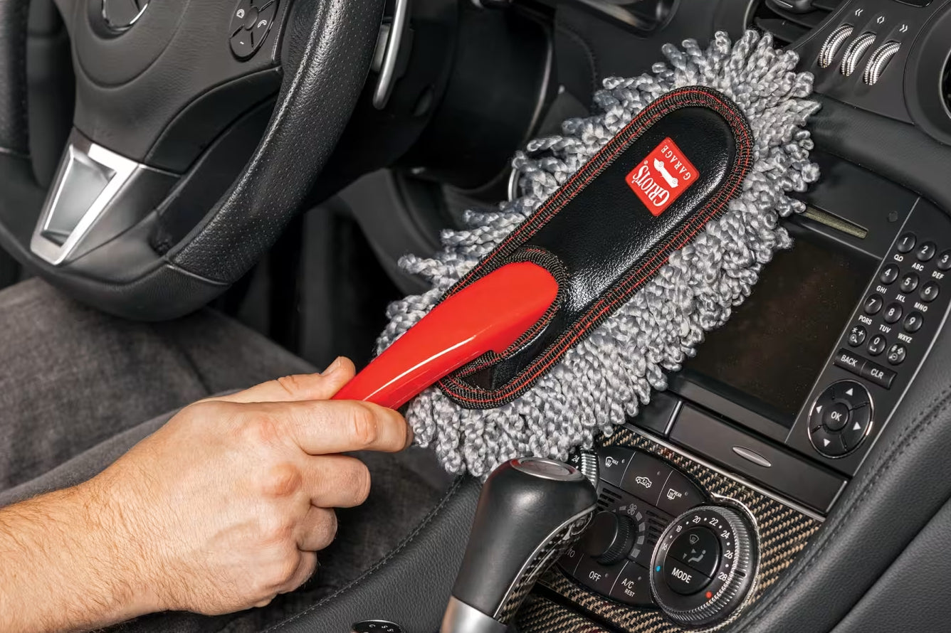 Person cleaning car interior with a red brush and gray microfiber towel.