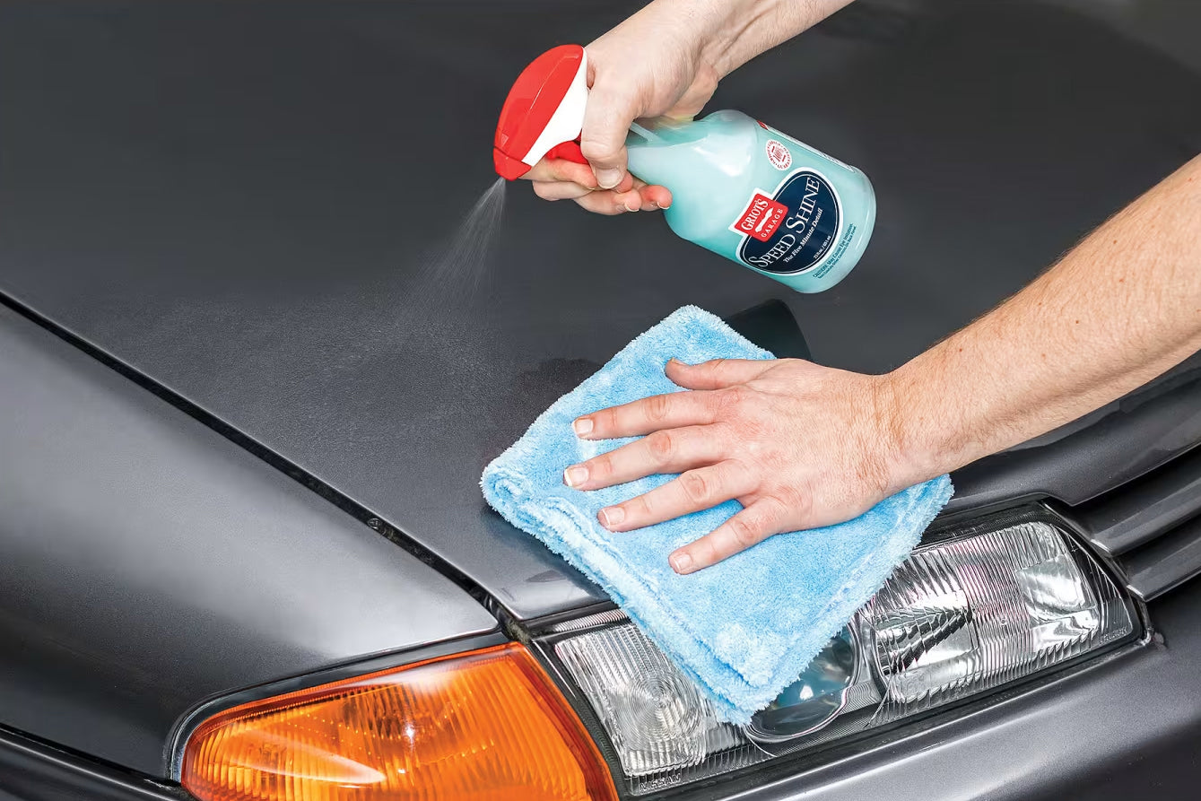 Person cleaning a car's hood with a spray bottle and microfiber cloth.