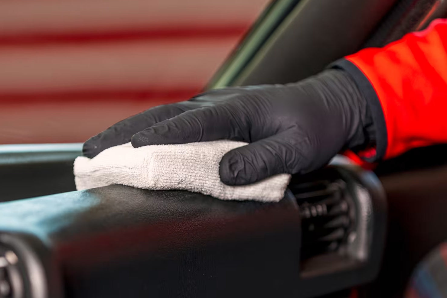Person cleaning a car's interior with a cloth and black gloves