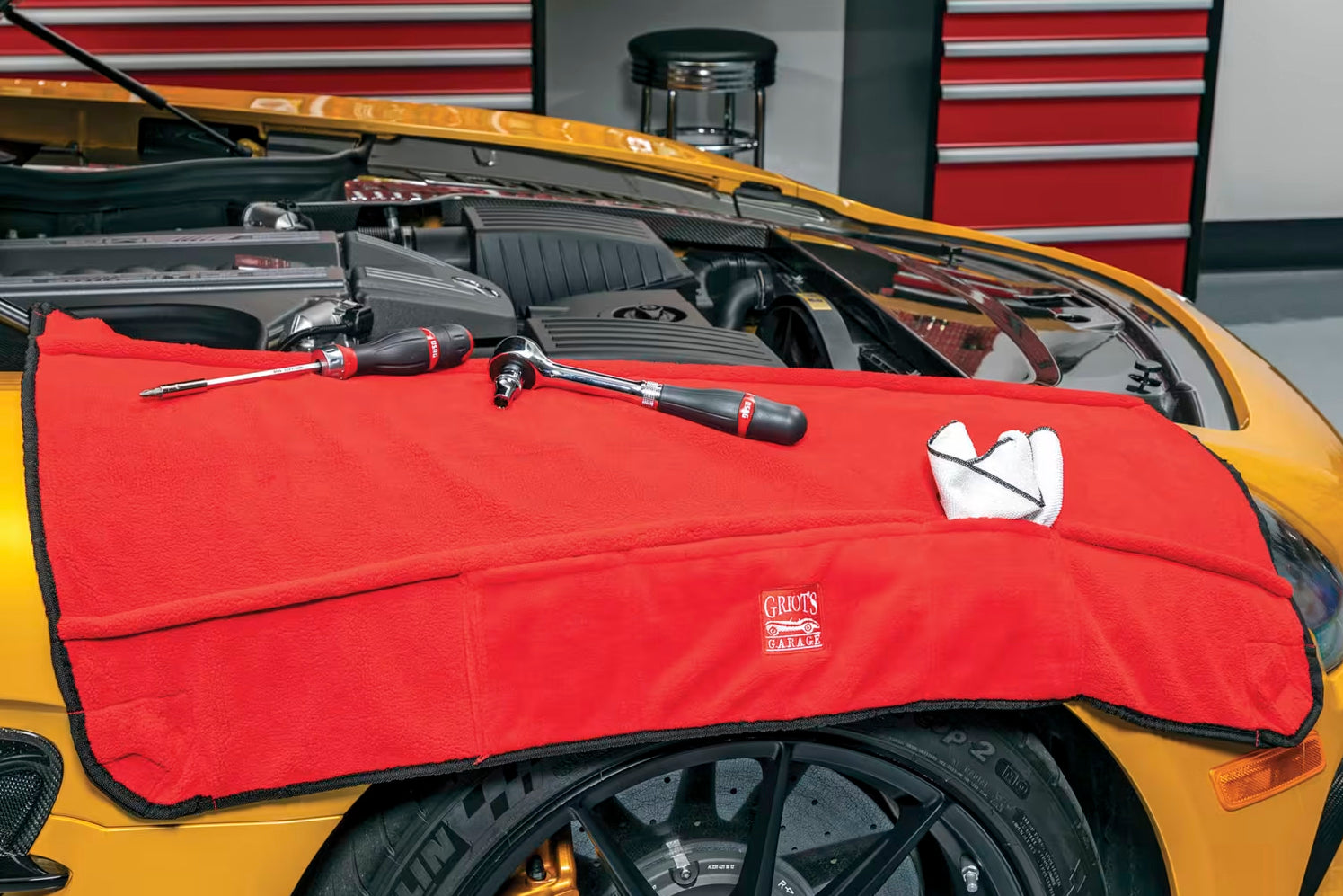 Red car cover with tools on a yellow car in a garage setting