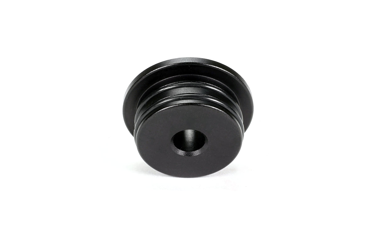 Single PERRIN GR Corolla Shifter Cable Bushing on white background, black anodized aluminum with machined grooves, bottom face view.